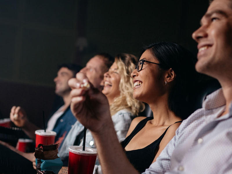 Group of people in theater with popcorn and drinks. Young friends watching movie in cinema.